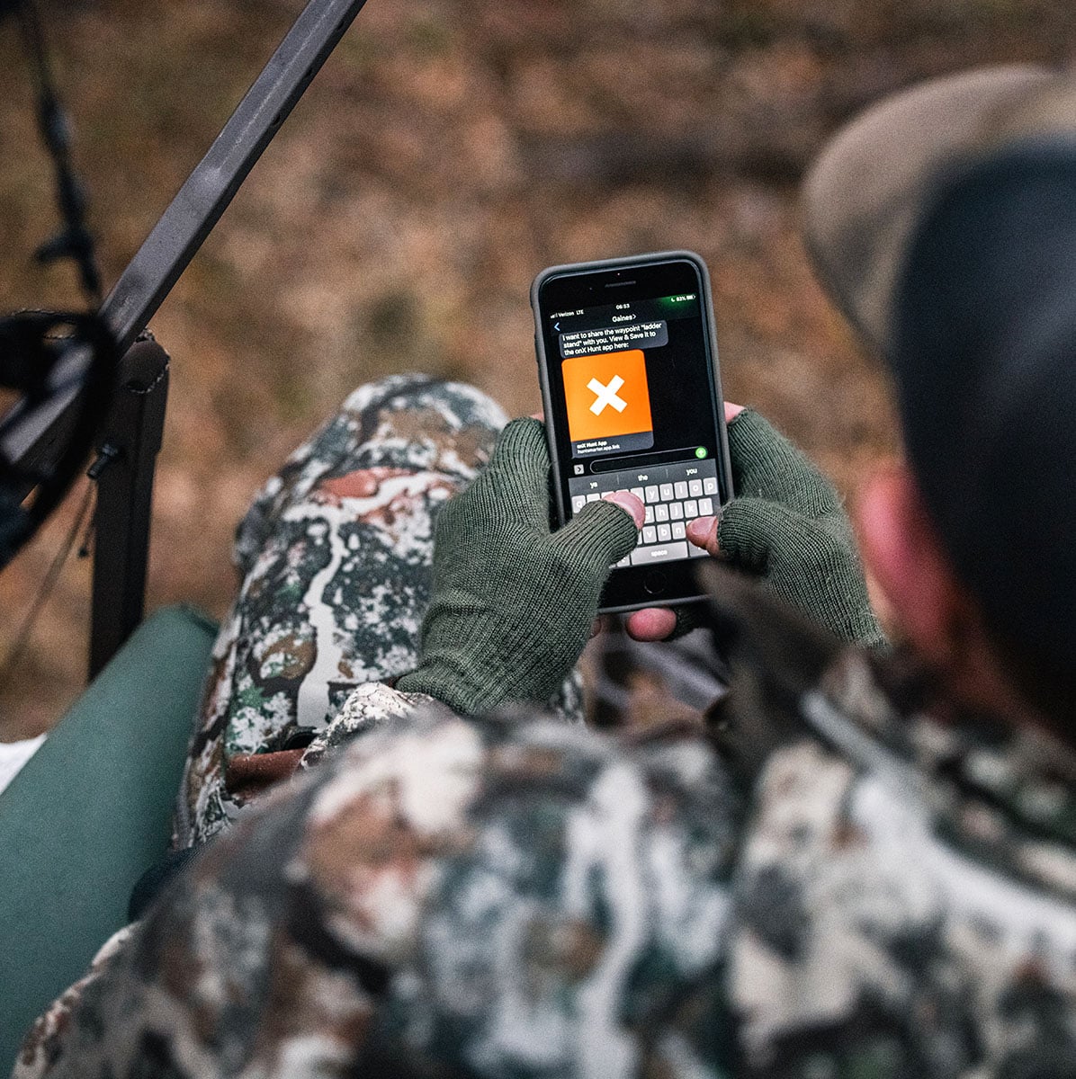 A deer hunter looking at his cell phone in the stand.